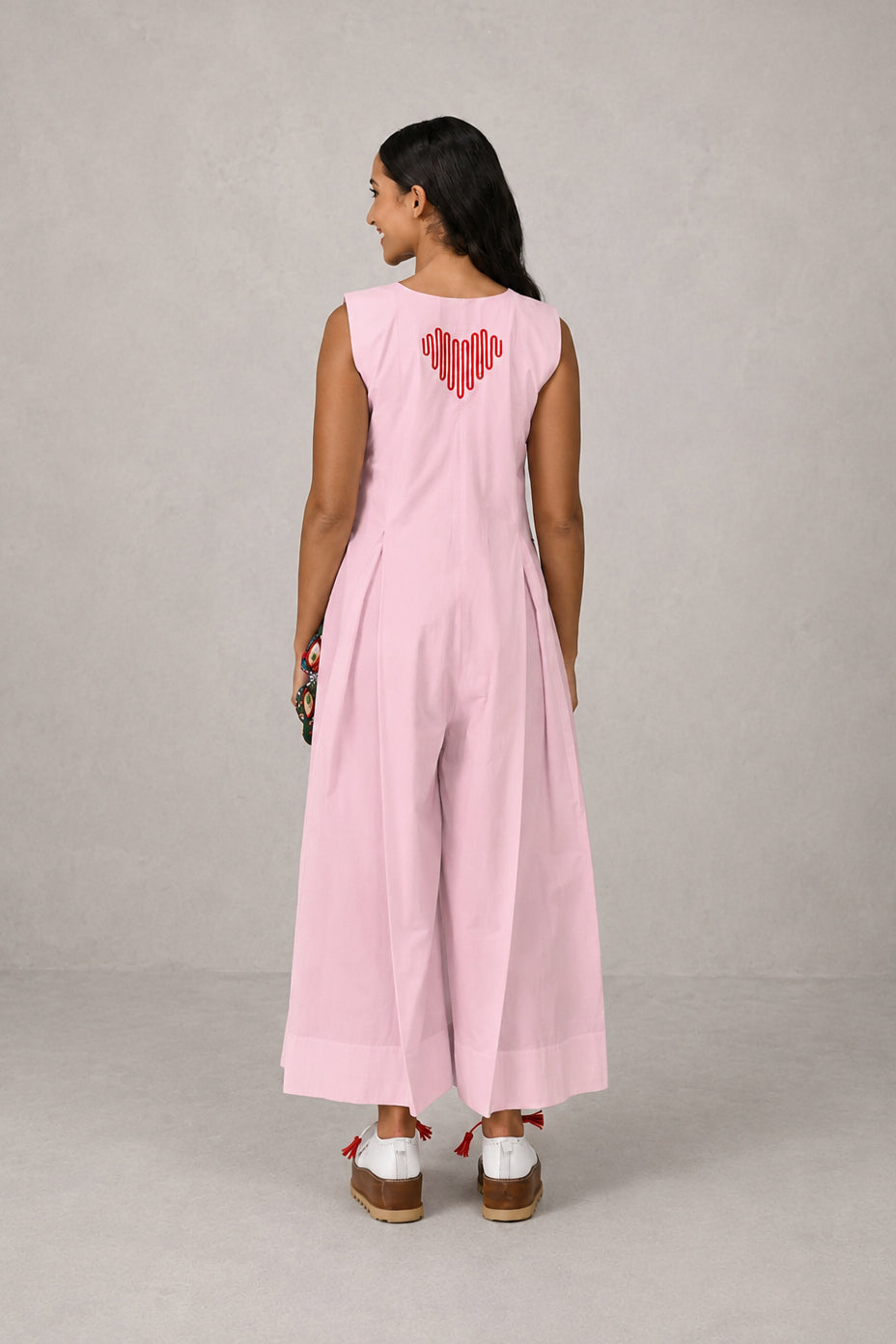 Woman wearing a pink sleeveless jumpsuit with a heart design on the back against a gray background
