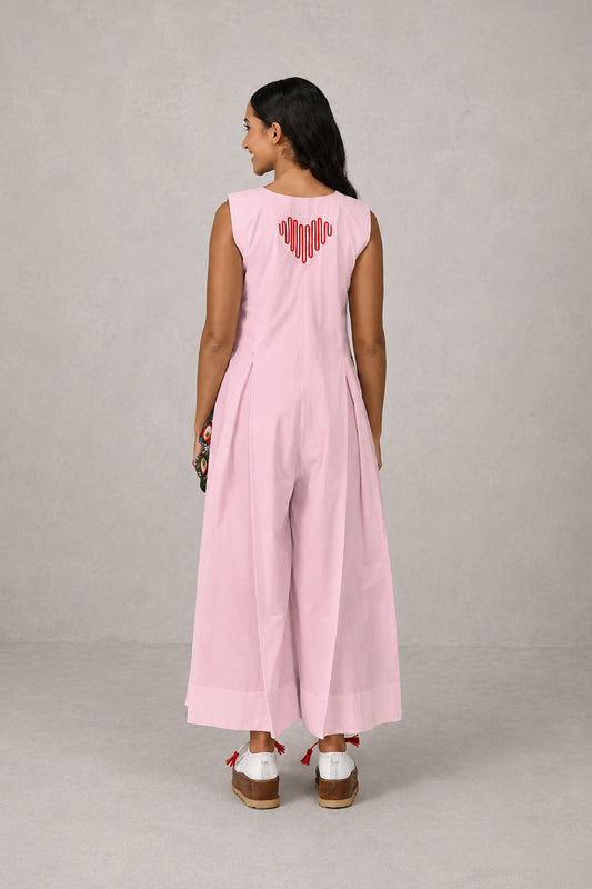 Woman wearing a pink sleeveless jumpsuit with a heart design on the back against a gray background