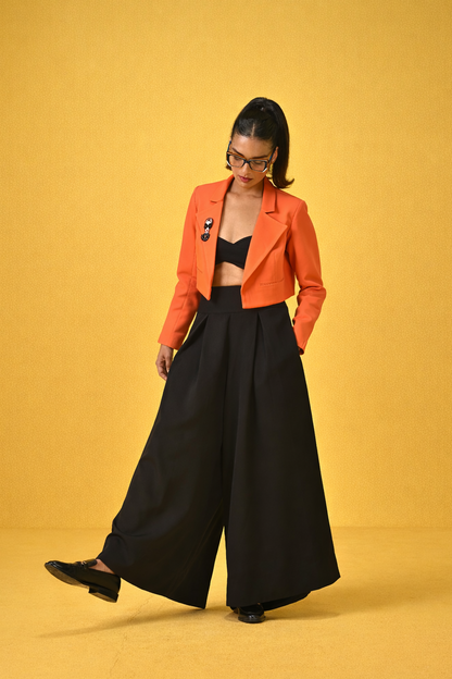 Woman wearing an orange jacket and black pants on a yellow background