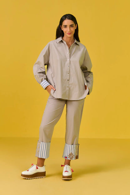 Woman wearing a beige outfit with cuffed pants on a yellow background