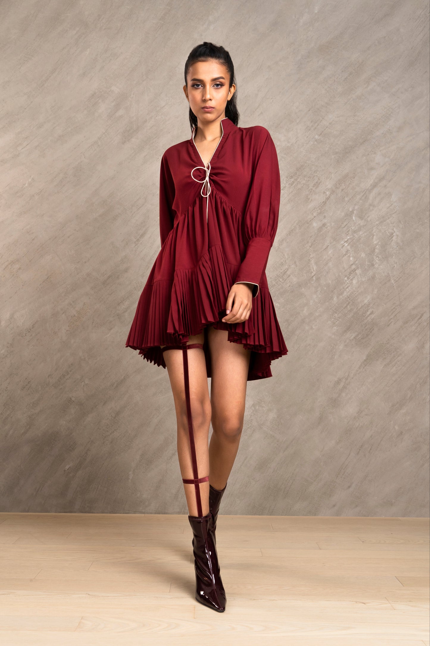 Woman wearing a burgundy dress and boots against a neutral background