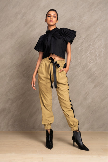 A model wearing a black structural cross body top with short sleeves and pleated details on the shoulder sleeves, paired with beige CROFT pants.